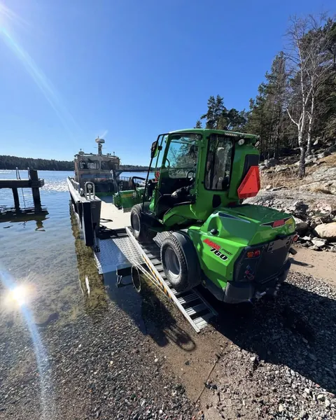 Arbetsbåten BOB lastad med grön hjullastare på klippig strand